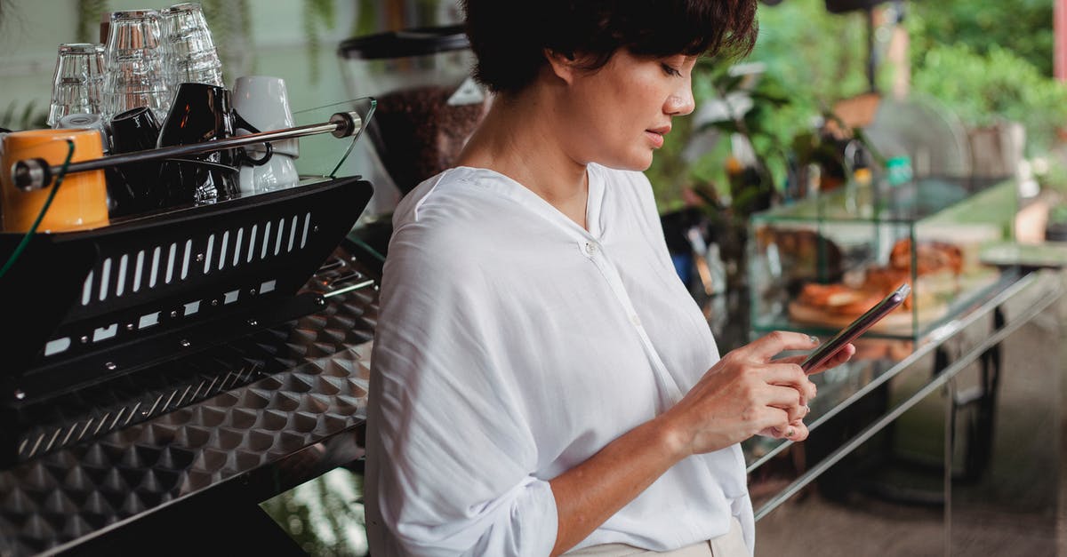 Hong Kong restaurant apps/websites - Side view of charming ethnic female in stylish clothes browsing mobile phone while leaning on professional coffee machine in cafe