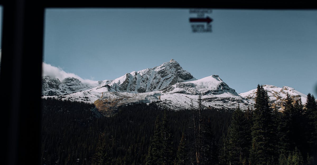 How can a Green Card holder prove their length of absence when exiting and entering through a Mexican land crossing? - Through glass view of high mountains covered with snow near green woods under blue cloudless sky in nature