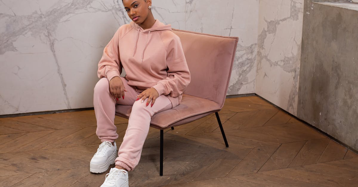 How can I be assured a seat on the plane? - Full body of trendy African American female wearing stylish hoodie and pants looking at camera while sitting on armchair against wall How can I be assured a seat on the plane? - Full body of trendy African American female wearing stylish hoodie and pants looking at camera while sitting on armchair against wall