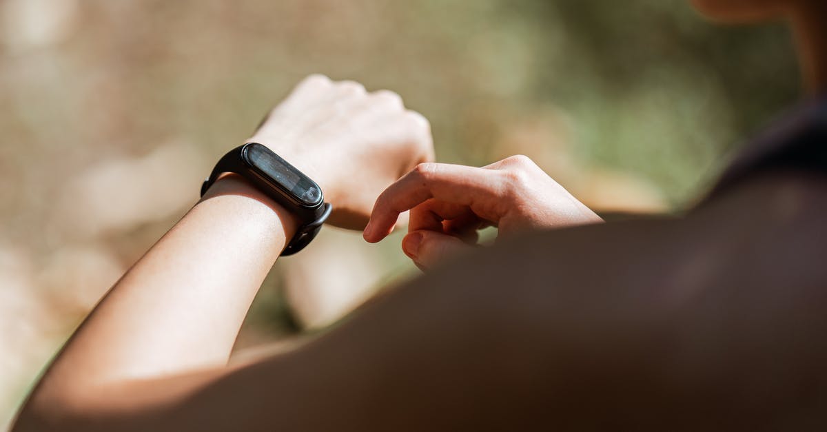 How can I determine if it is possible to check luggage during a layover? - From behind crop anonymous sportswoman checking notifications on  modern fitness tracker while training against blurred nature background on sunny weather