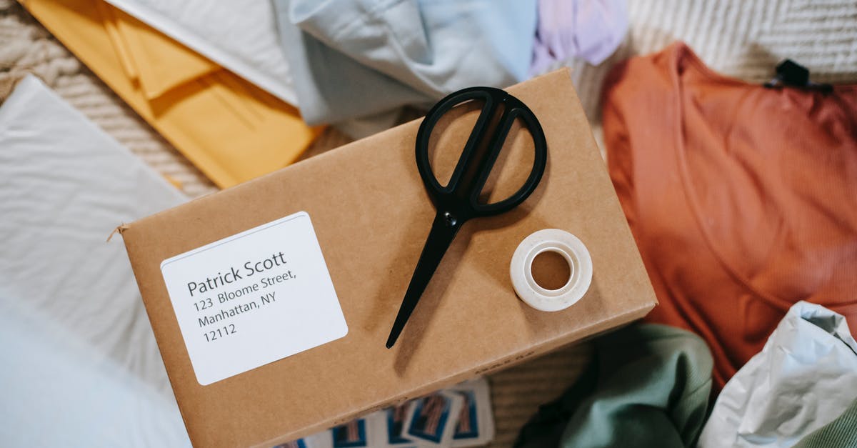 How can I find out how many Miles I will receive on Royal Plus? - Top view of tape with scissors on carton box with exact address and name among clothes How can I find out how many Miles I will receive on Royal Plus? - Top view of tape with scissors on carton box with exact address and name among clothes