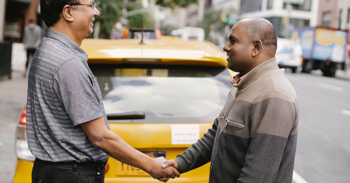 How can I meet the world's most jovial taxi driver? - Side view of smiling ethnic men shaking hands and greeting each other while standing on street near taxi car How can I meet the world's most jovial taxi driver? - Side view of smiling ethnic men shaking hands and greeting each other while standing on street near taxi car