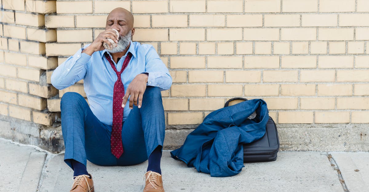 How can I respectfully greet in Thailand? - Full body of mature African American bearded businessman in blue trousers and light shirt with maroon tie sitting on ground at brick wall and drinking beverage from tin can How can I respectfully greet in Thailand? - Full body of mature African American bearded businessman in blue trousers and light shirt with maroon tie sitting on ground at brick wall and drinking beverage from tin can