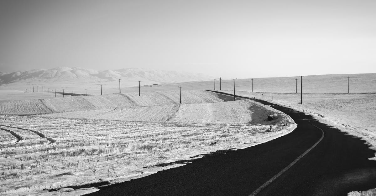 How can I travel to the north pole (Arctic areas) from Russia cheaply? [duplicate] - Black and white of empty asphalt roadway running through mountainous terrain with fields covered with snow