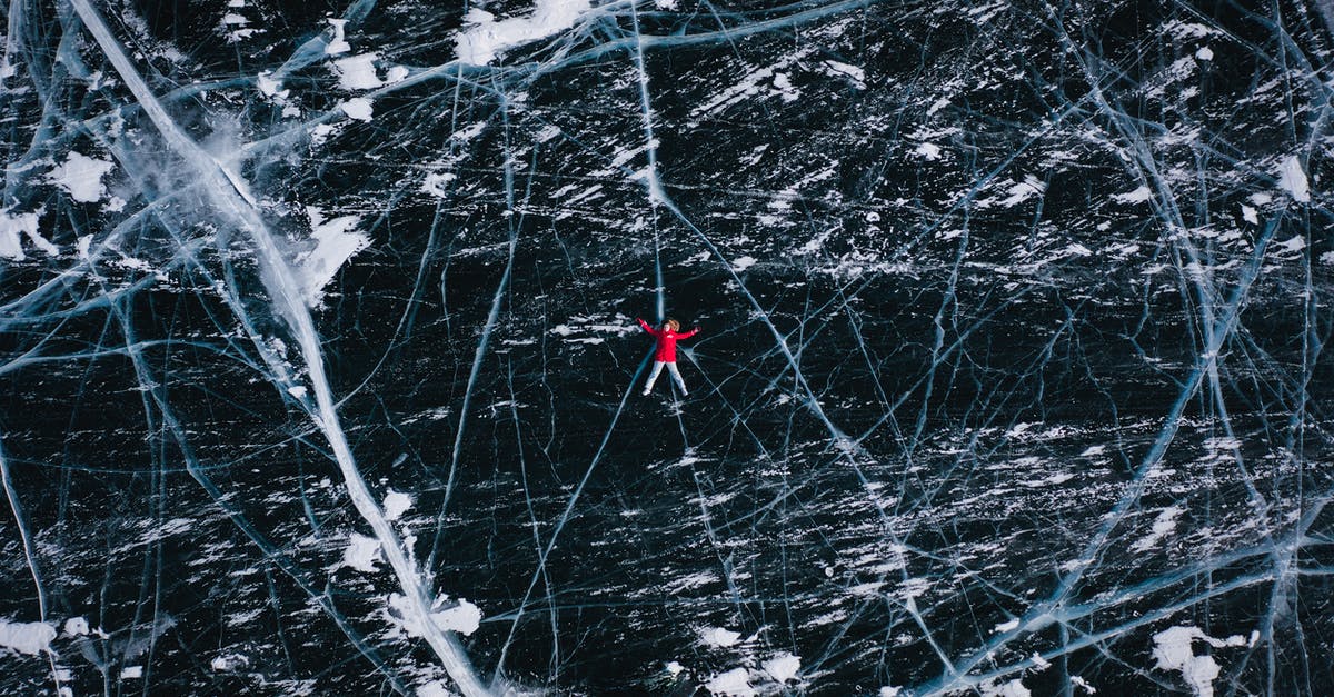How can I travel to the north pole (Arctic areas) from Russia cheaply? [duplicate] - Drone view of anonymous tourist lying on frozen river with cracks during winter trip in daytime