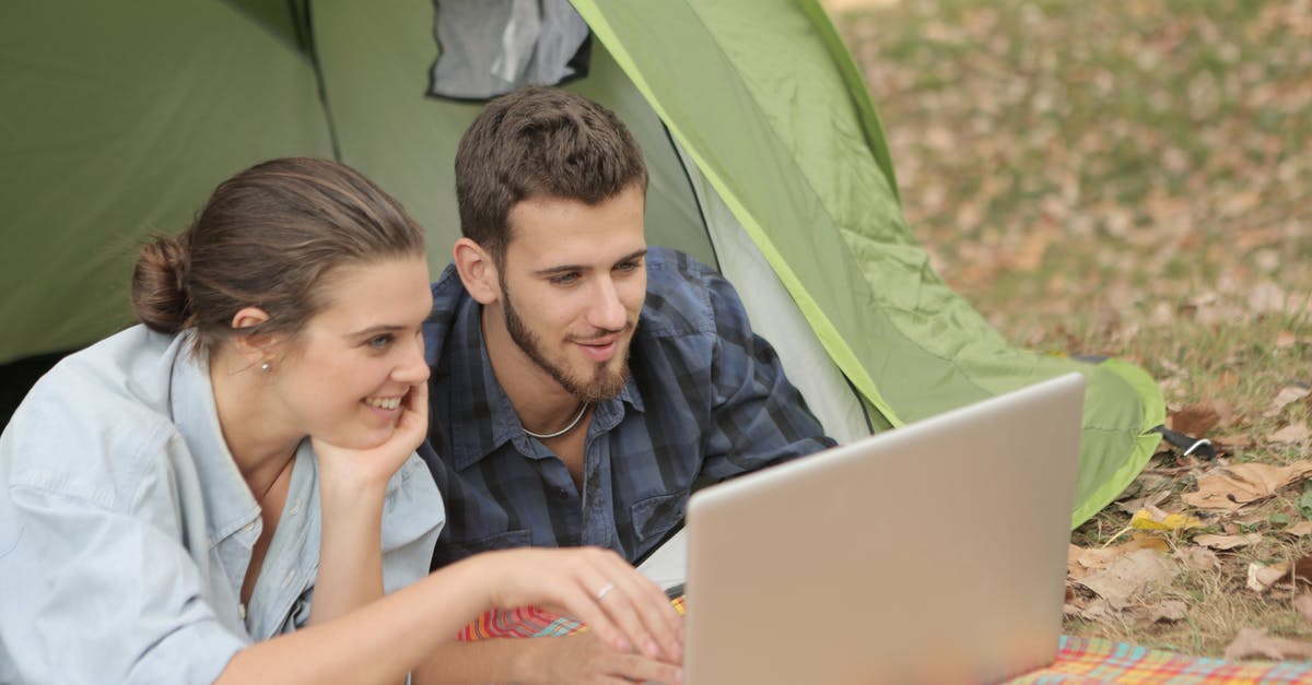 How can you enjoy nature, when it looks better in photographs than in person? [closed] - Cheerful female and bearded male using laptop with touchpad while resting in tent at campsite