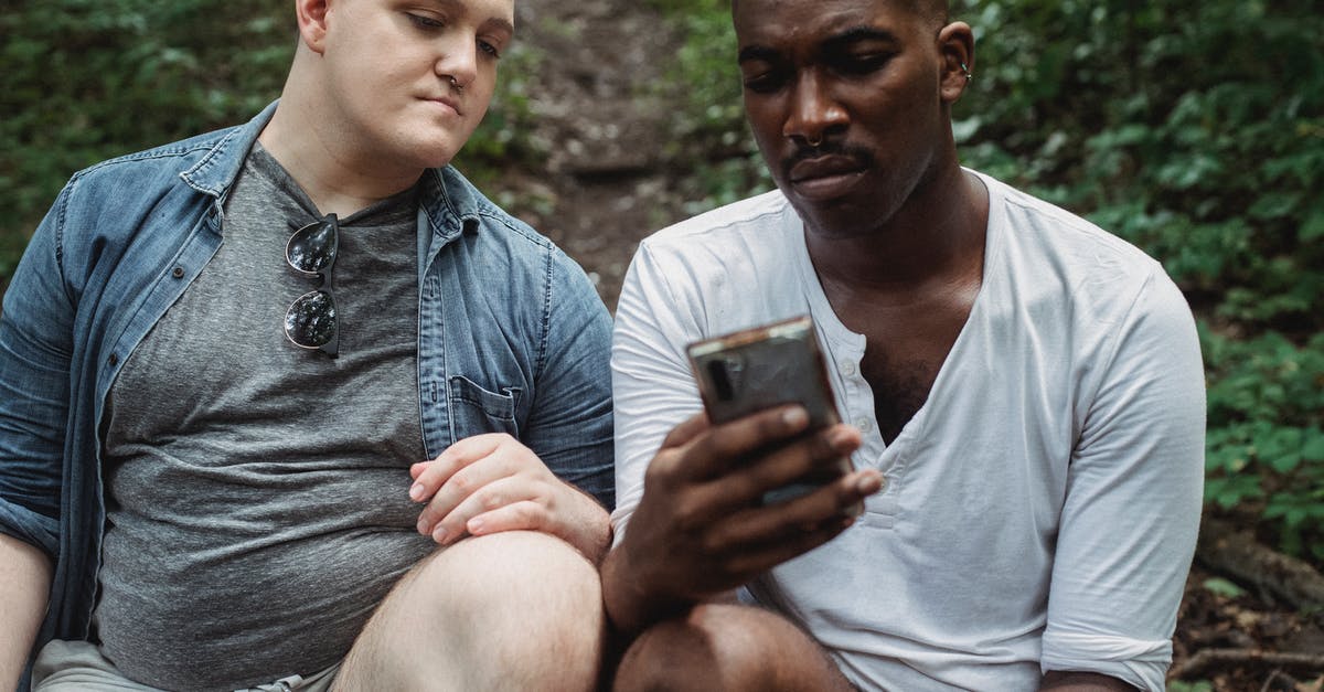 How common are such crooked forests and where can I find one? - Concentrated multiethnic male travelers surfing internet while relaxing in woodland in daytime on blurred background