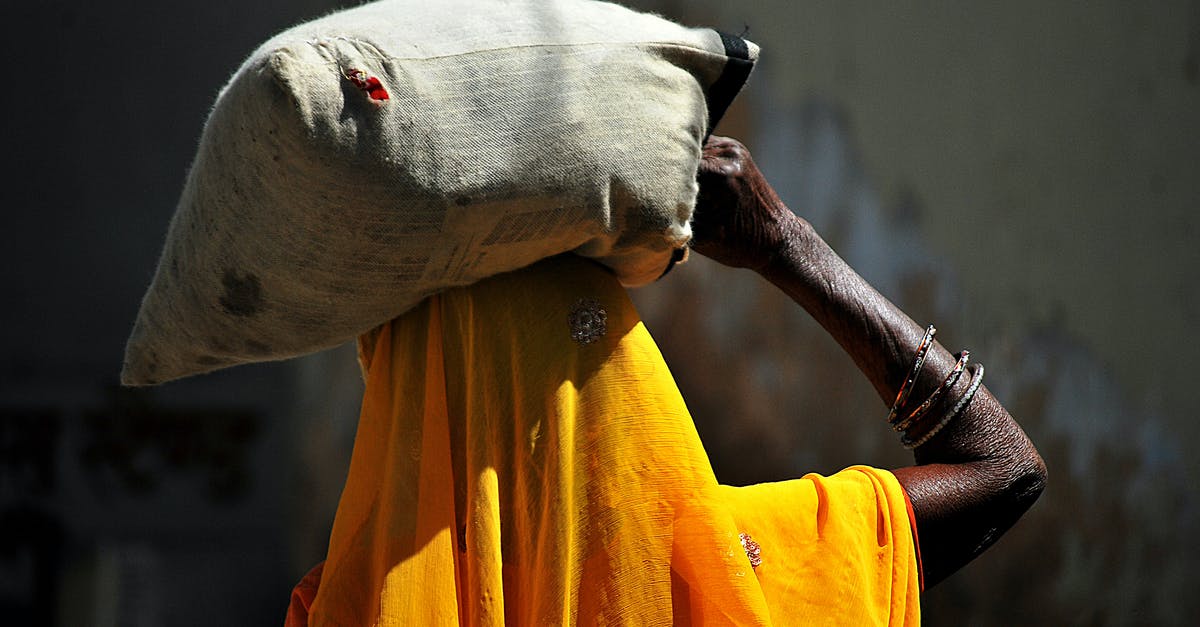 How do airlines compute weight allowances for carry-on bags? - Back view of unrecognizable African female in traditional yellow headscarf carrying heavy sack on head while walking in village on sunny day How do airlines compute weight allowances for carry-on bags? - Back view of unrecognizable African female in traditional yellow headscarf carrying heavy sack on head while walking in village on sunny day