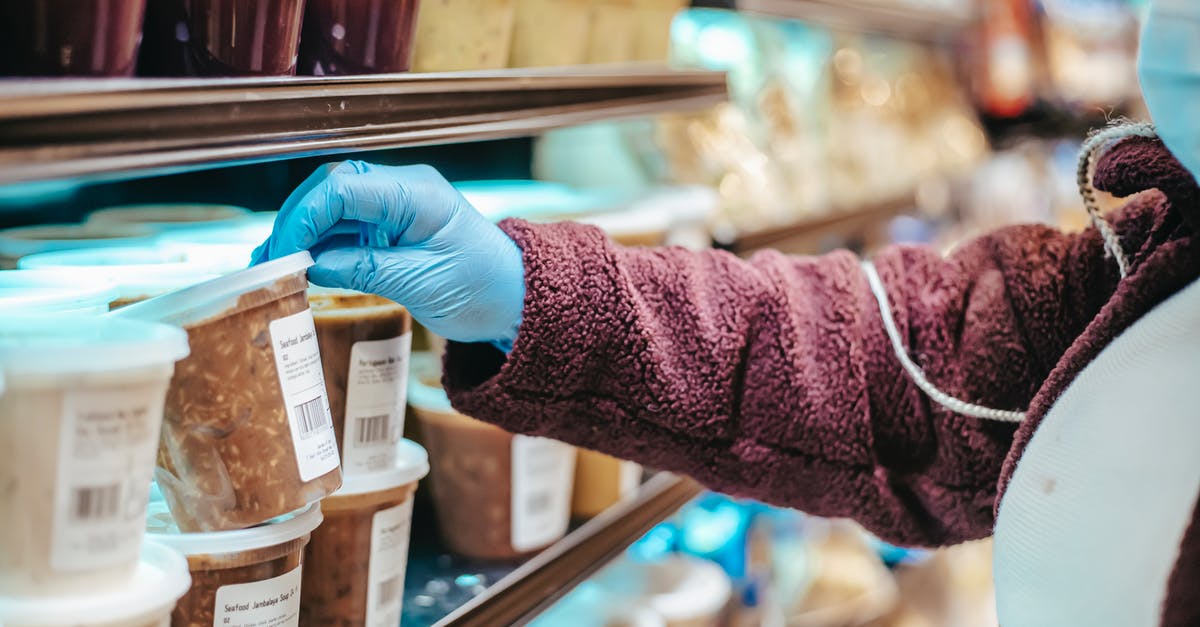 How do airports check incoming goods [closed] - Crop anonymous female customer in protective mask reading label on frozen food in plastic container in grocery store