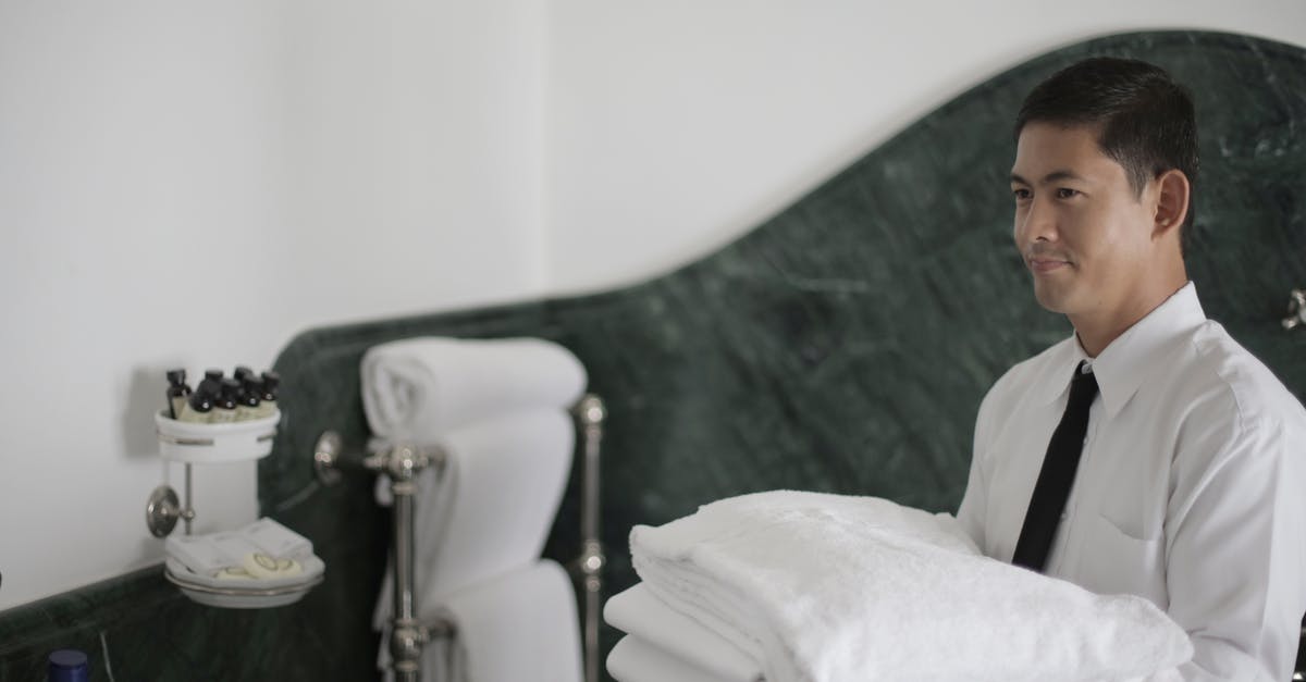 How do hotel housekeepers know if a room is in use? - Side view of smiling ethnic male hotel employee holding stack of clean white towels while cleaning bathroom How do hotel housekeepers know if a room is in use? - Side view of smiling ethnic male hotel employee holding stack of clean white towels while cleaning bathroom