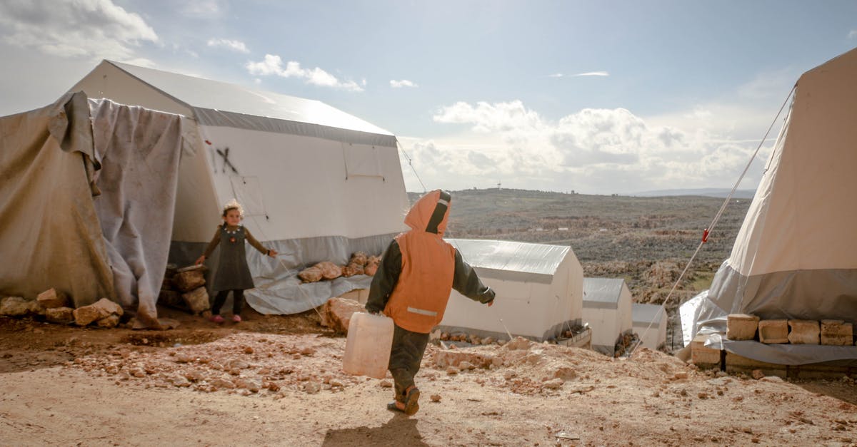 How do I find an immigration lawyer/solicitor to help with my UK Visa application? - Anonymous boy carrying heavy plastic canister while poor girl watching near tents under cloudy sunny sky