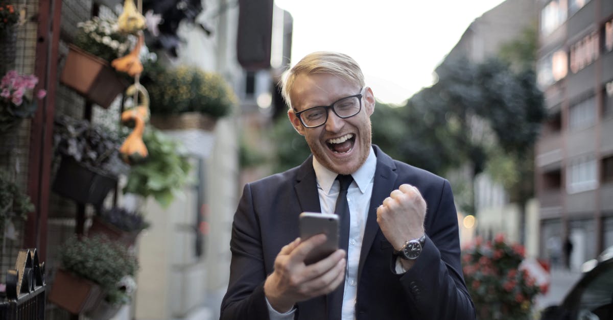 How do I get the most use of my BA Executive Club membership with QatarAirways? [closed] - Excited young man in formal wear and eyeglasses clenching fist and rejoicing victory while using mobile phone in modern city street