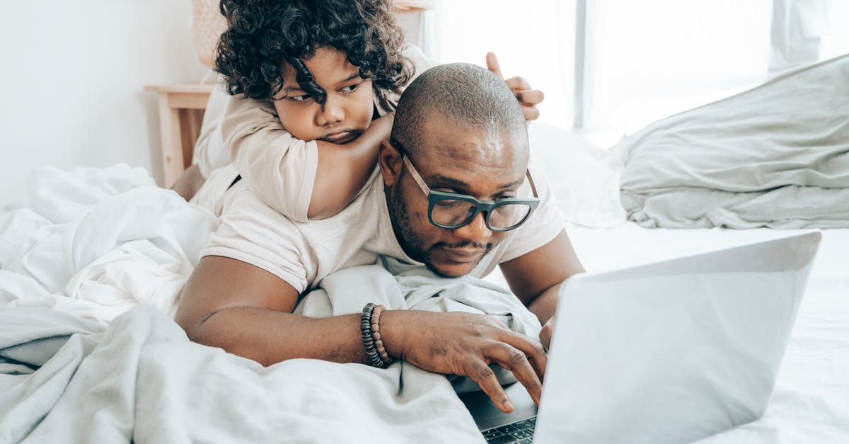 How do I identify an airport’s official free Wi-Fi network? - Focused black man with kid surfing laptop on bed