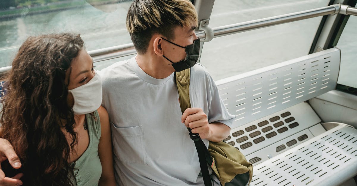 How do I mask my location while traveling so I can use geo blocked services? [closed] - Positive couple wearing casual clothes and protective face masks embracing and riding ropeway cabin above contemporary city river