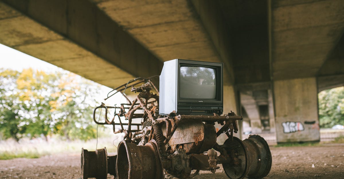 How do I prevent damage to electronic devices at airport security? - Old damaged vehicle with vintage television set on rough pathway under bridge in sunlight