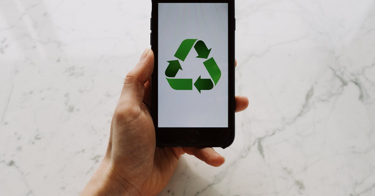 How do I prevent damage to electronic devices at airport security? - From above view of faceless person holding mobile phone with white screen and green recycle logo above marble surface