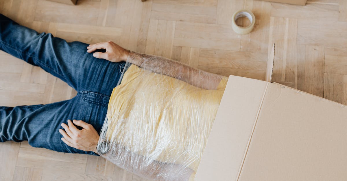 How do I prevent my head from drooping while trying to sleep on a plane? - From above anonymous male in casual clothing lying on parquet with box on head and upper body wrapped in clingy plastic tape during moving out How do I prevent my head from drooping while trying to sleep on a plane? - From above anonymous male in casual clothing lying on parquet with box on head and upper body wrapped in clingy plastic tape during moving out