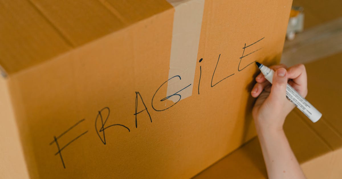How do I transport fragile items? - From above of crop unrecognizable person writing with marker on cardboard box with fragile products before relocation How do I transport fragile items? - From above of crop unrecognizable person writing with marker on cardboard box with fragile products before relocation
