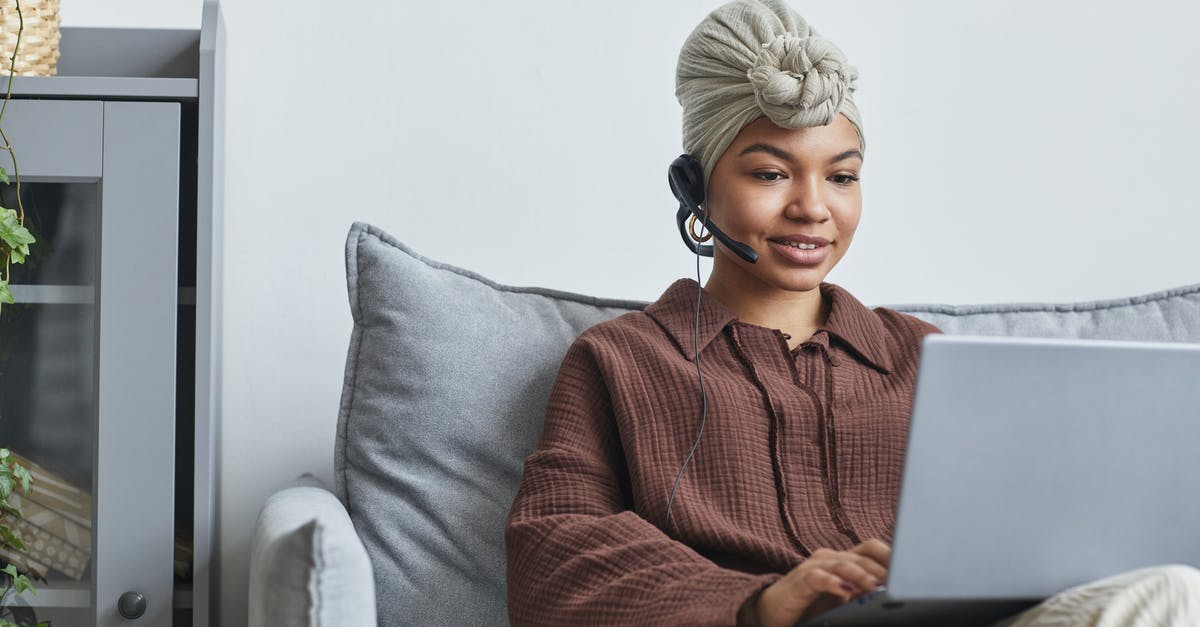 How do you call a local service number, when abroad? - Focused African American female call agent with handsfree headset typing on netbook while sitting on couch near cupboard in light room How do you call a local service number, when abroad? - Focused African American female call agent with handsfree headset typing on netbook while sitting on couch near cupboard in light room