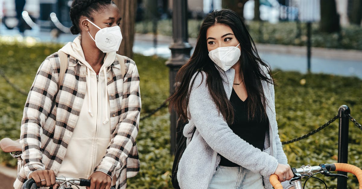 How is Venice during COVID times? - Multiethnic girlfriends in masks talking to each other while strolling with bicycles in park during COVID pandemic How is Venice during COVID times? - Multiethnic girlfriends in masks talking to each other while strolling with bicycles in park during COVID pandemic