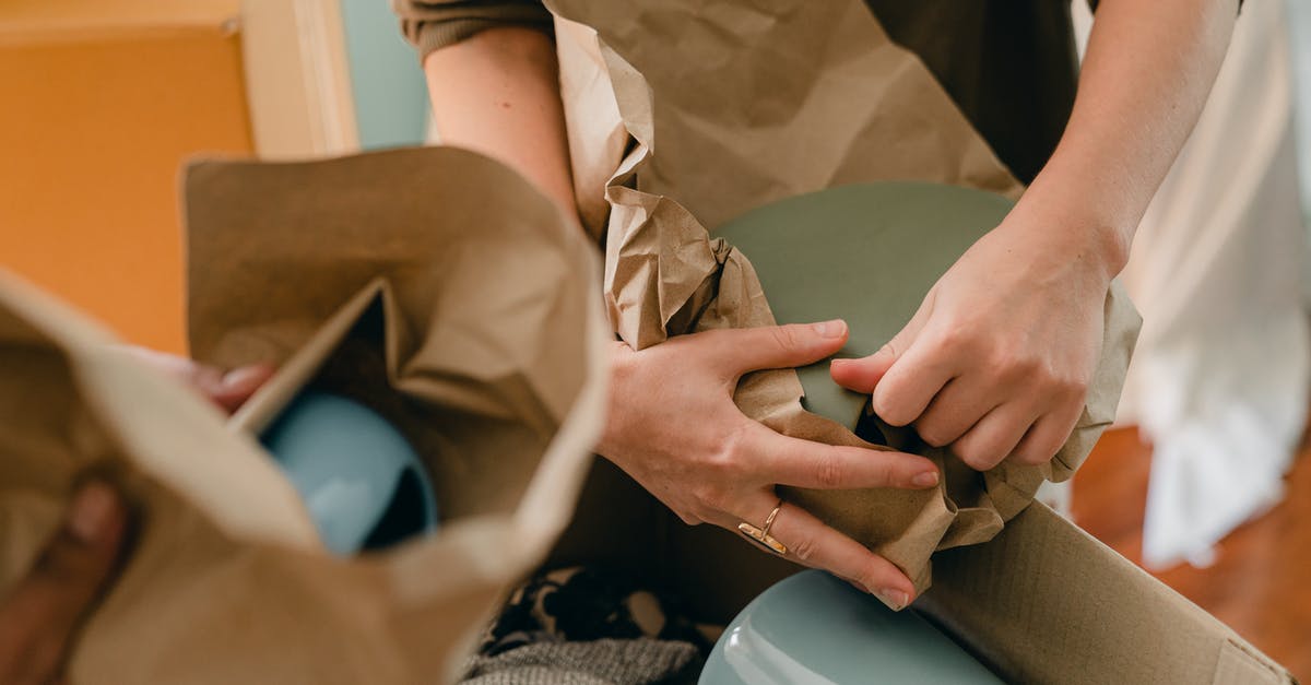 How many laptops are allowed in hand baggage in European flight? - Crop unrecognizable person packing ceramic tableware in parchment