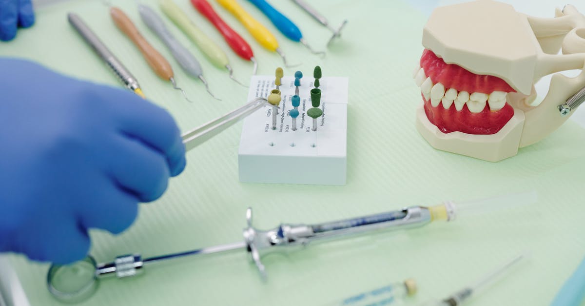 How many laptops are allowed in hand baggage in European flight? - From above of crop faceless orthodontist in latex gloves and tweezers working at medical table with cast jaw and set of syringes near periodontal scalers