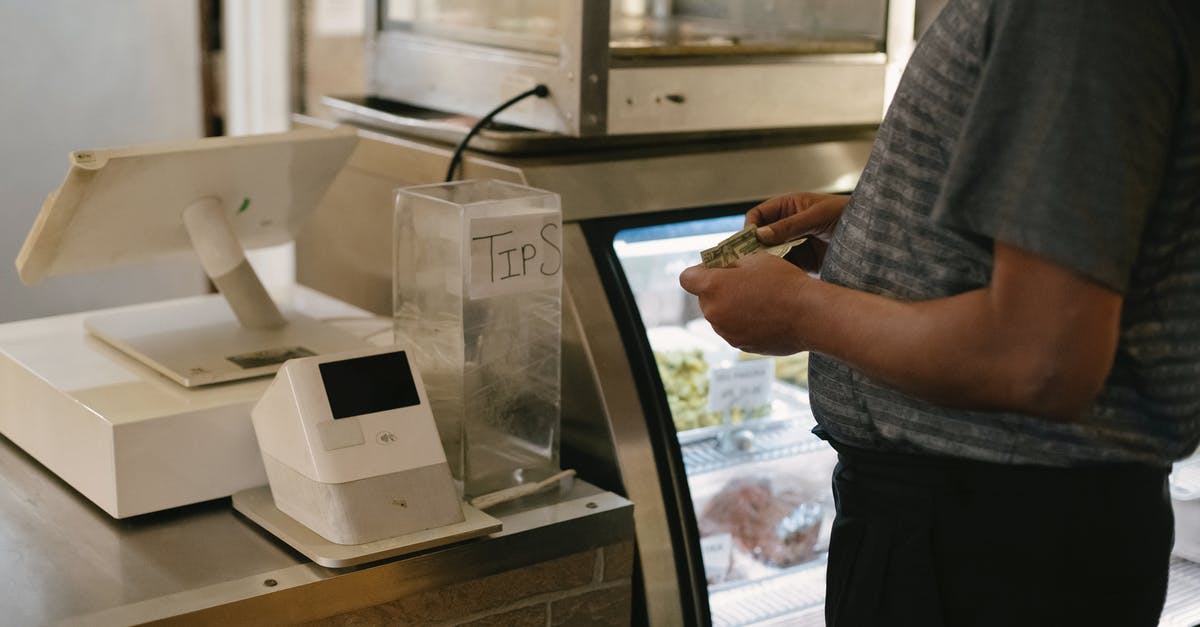 How much do extra kilos of check-in luggage cost in general? - Unrecognizable male in casual clothes standing with money near cash register in grocery store while making purchase near glass showcase How much do extra kilos of check-in luggage cost in general? - Unrecognizable male in casual clothes standing with money near cash register in grocery store while making purchase near glass showcase