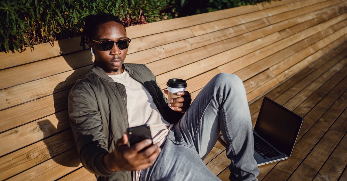 How much time does it take to go from Tamsui to Yehliu by bus along the coast? - From above of young black male in trendy wear and sunglasses relaxing on wooden bench in park with coffee to go and laptop and taking selfie on mobile phone