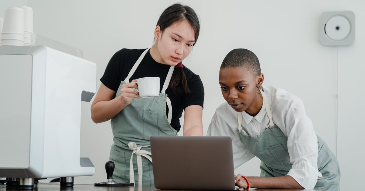 How should I explain a previous refusal in a new UK visa application? - Serious Asian female barista with coffee in hand teaching new black colleague to use computer program while standing at table with laptop