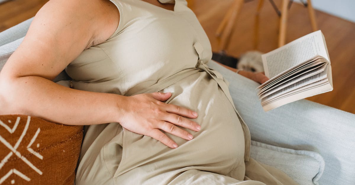 How to book a ticket for an unborn infant? - Faceless pregnant female in beige dress reading book on comfortable sofa and touching tummy How to book a ticket for an unborn infant? - Faceless pregnant female in beige dress reading book on comfortable sofa and touching tummy
