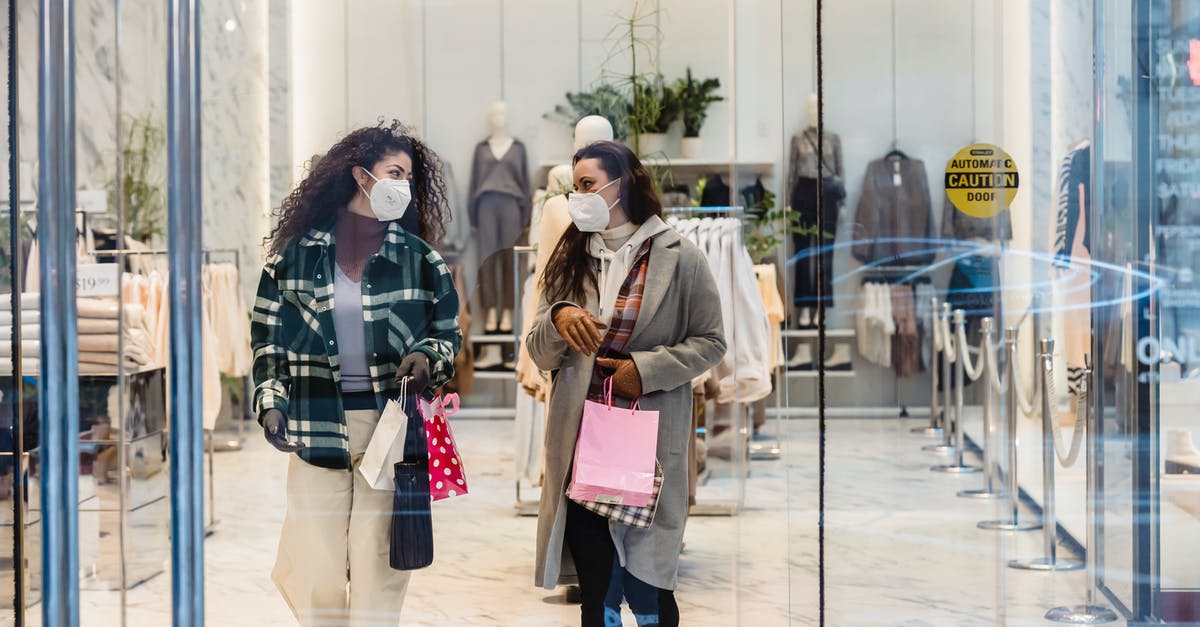 How to buy duty free other than at the airport? - Through glass of female friends in protective masks carrying shopping bags while walking out of clothing store How to buy duty free other than at the airport? - Through glass of female friends in protective masks carrying shopping bags while walking out of clothing store