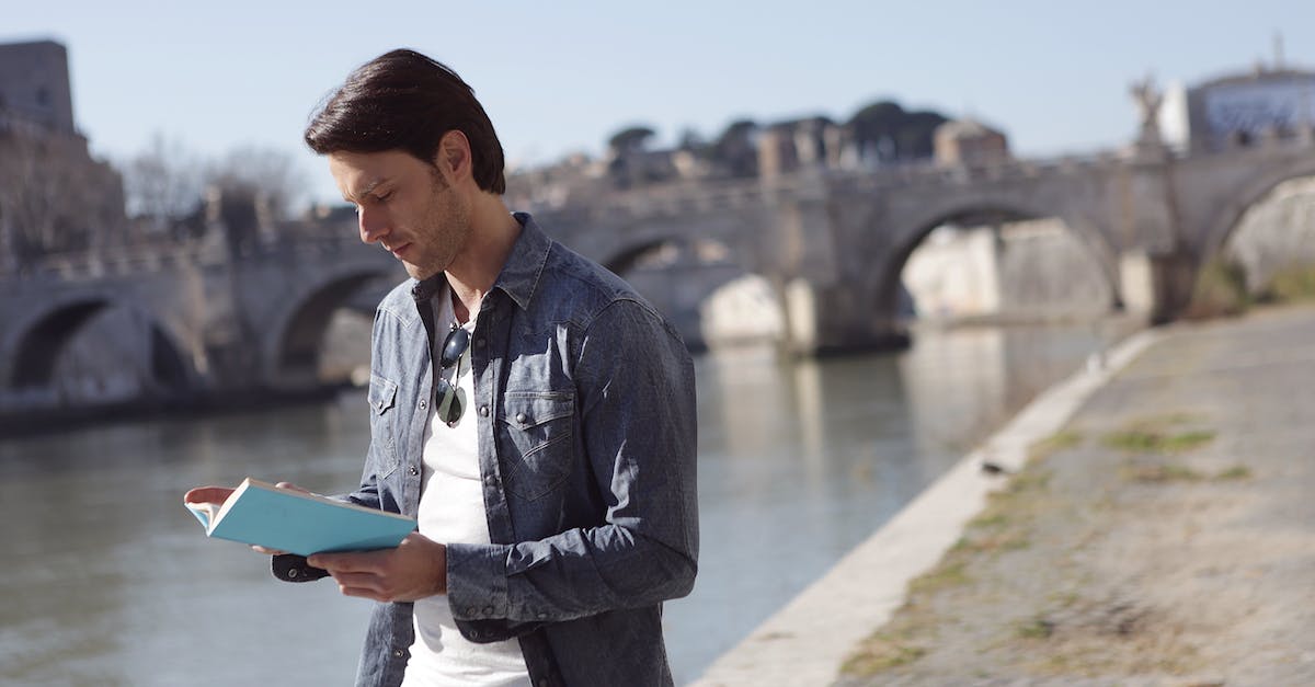 How to document travel expenses? - Young Man in Denim Jacket is Reading a Book Near River Side How to document travel expenses? - Young Man in Denim Jacket is Reading a Book Near River Side