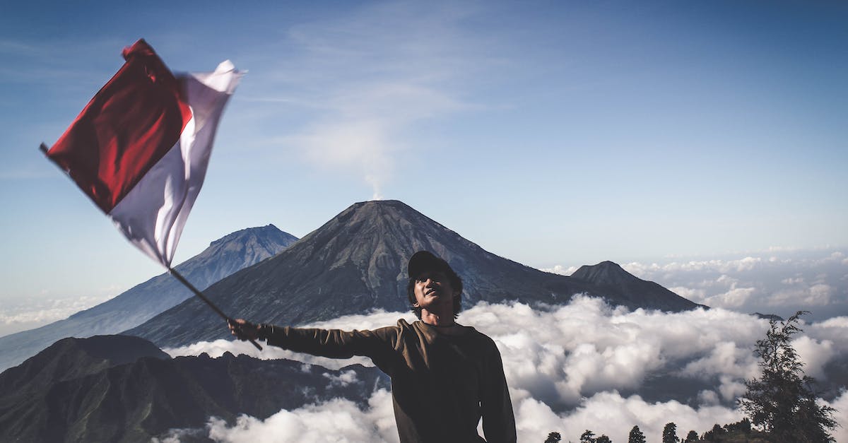 How to extend Indonesian visa on arrival (VOA) in Indonesia - Man Wearing Black Crew-neck Sweater Holding White and Red Flag Standing Near Mountain Under Blue and White Sky How to extend Indonesian visa on arrival (VOA) in Indonesia - Man Wearing Black Crew-neck Sweater Holding White and Red Flag Standing Near Mountain Under Blue and White Sky