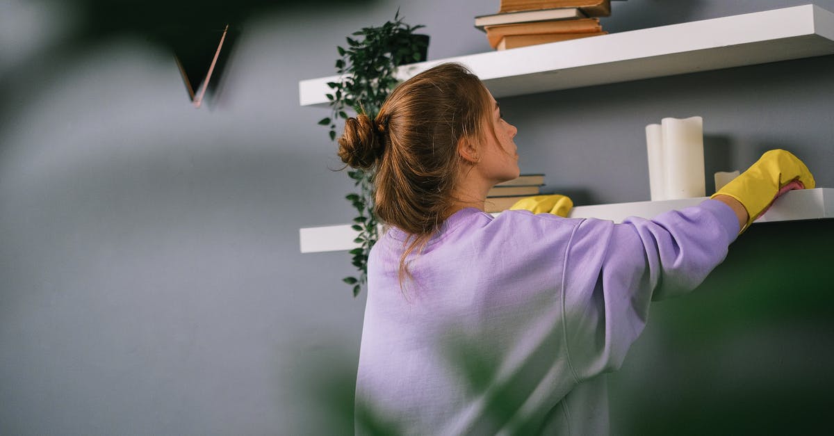 How to find accommodation when what you reserved appears to be overbooked, or worse, non-existent? - Young female wiping shelves in room with gray wall