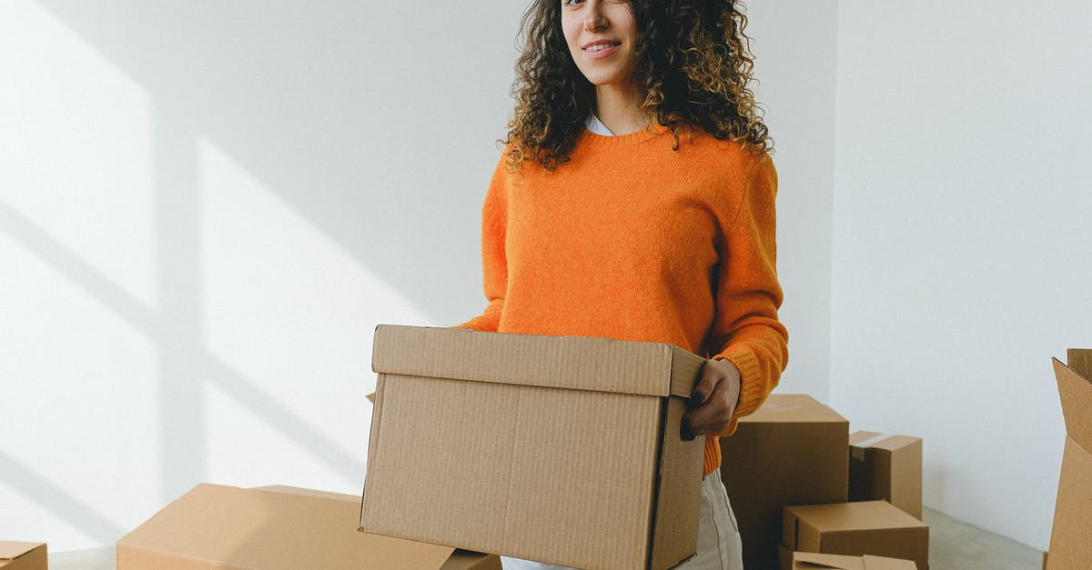 How to find accommodation when what you reserved appears to be overbooked, or worse, non-existent? - Young female arranging carton box and smiling at camera during relocation