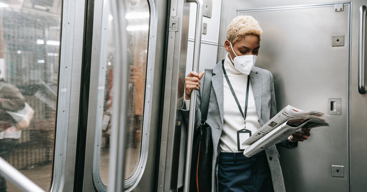 How to get updated about current incidents and safety concerns? - Concentrated young African American female in formal outfit and protective mask reading fresh newspaper while standing in metro train corner How to get updated about current incidents and safety concerns? - Concentrated young African American female in formal outfit and protective mask reading fresh newspaper while standing in metro train corner