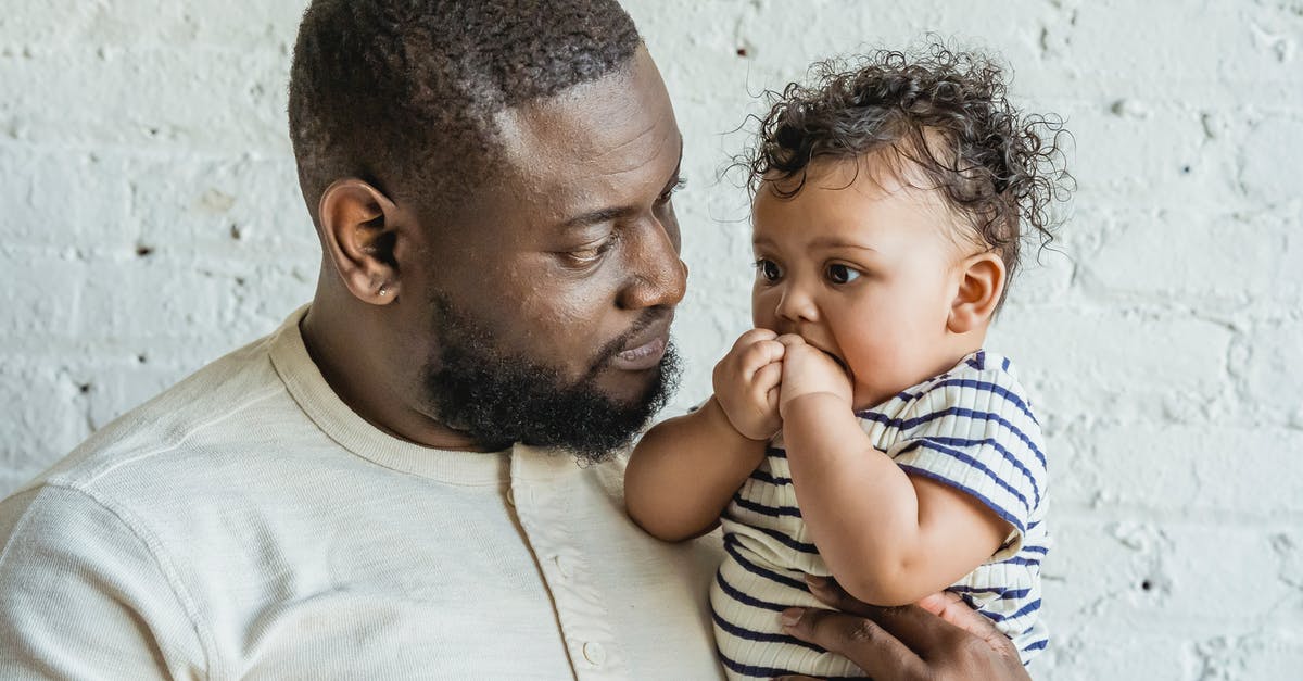 How to pass the time on a six-hour layover with small children (in Frankfurt)? [closed] - Caring African American bearded man looking at little black toddler in arms while standing near white wall in light room