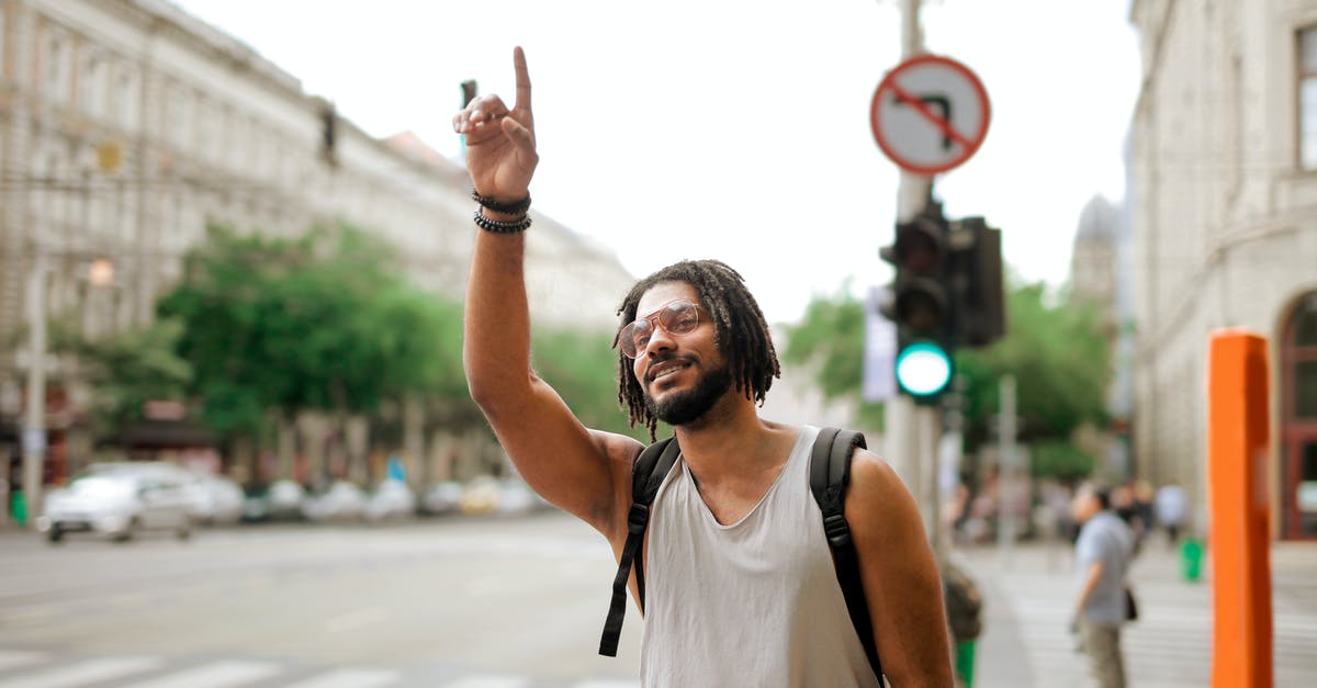 How to plan a road trip with stops on specific dates - Happy ethnic man with backpack hailing taxi on street How to plan a road trip with stops on specific dates - Happy ethnic man with backpack hailing taxi on street