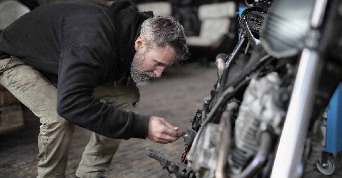 How to process a UK Visa if the owner of the business died [closed] - Side view of serious male master in untidy casual clothes standing near motorbike and checking details while working in garage