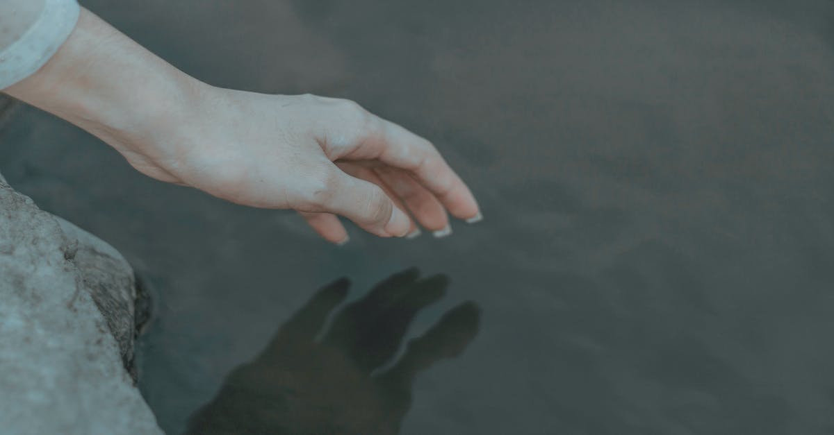 How to reach the clearest lake in the world? - Crop anonymous female on boulder on coast near pond touching peaceful water with hand in daylight How to reach the clearest lake in the world? - Crop anonymous female on boulder on coast near pond touching peaceful water with hand in daylight