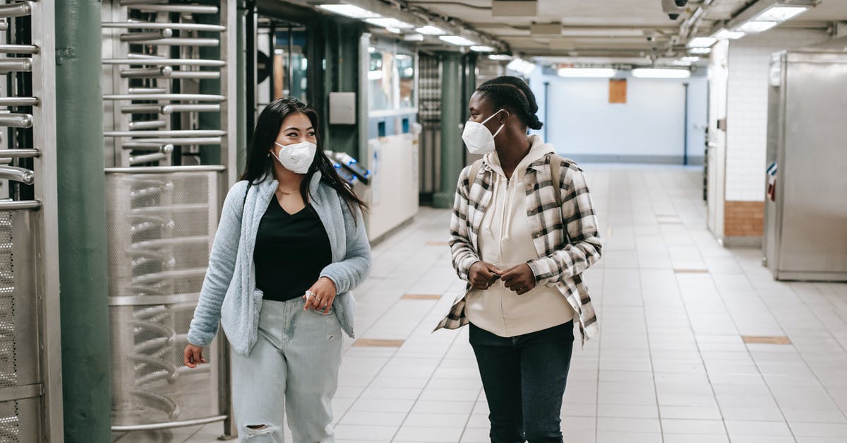 How to safely transport money? - Multiracial women in protective masks walking together in hallway of subway and looking at each other How to safely transport money? - Multiracial women in protective masks walking together in hallway of subway and looking at each other
