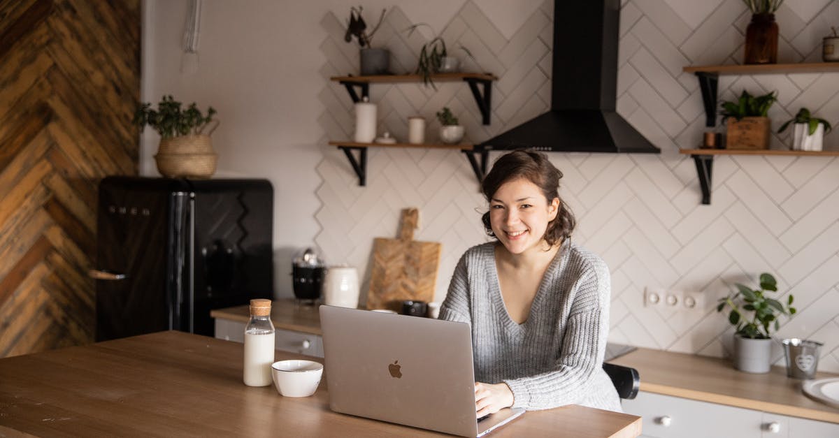 How to search for weekend flights? - Cheerful female in casual clothes sitting at table with laptop and bottle of milk while browsing internet on laptop during free time at home and smiling looking at camera How to search for weekend flights? - Cheerful female in casual clothes sitting at table with laptop and bottle of milk while browsing internet on laptop during free time at home and smiling looking at camera