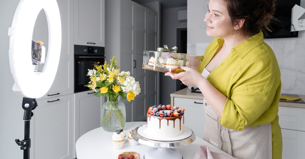 How to show share proceeds in bank statements for UK visa - Side view of positive young female food blogger in casual clothes and apron introducing yummy cakes and smiling while standing in front of ring lamp and recording vlog on smartphone