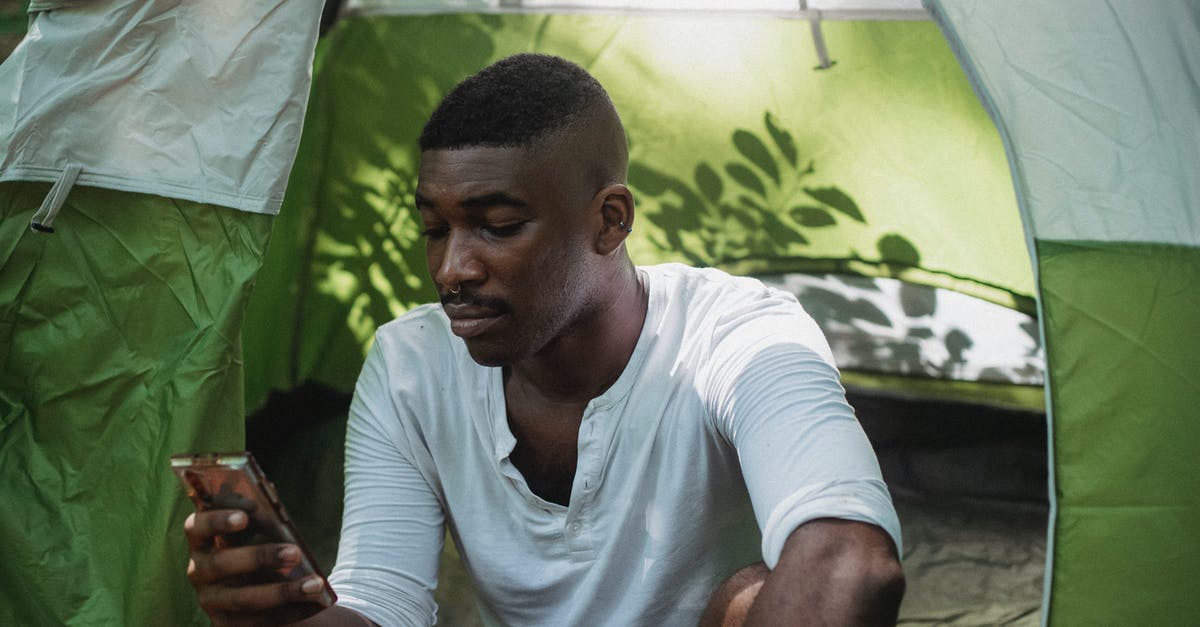 How to use trekking clothes? - Serious black man using smartphone in tent How to use trekking clothes? - Serious black man using smartphone in tent