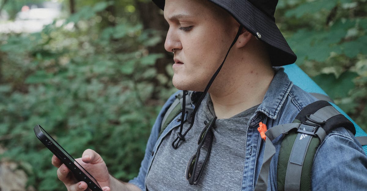 How to use trekking clothes? - Focused young male backpacker checking location on smartphone in nature How to use trekking clothes? - Focused young male backpacker checking location on smartphone in nature