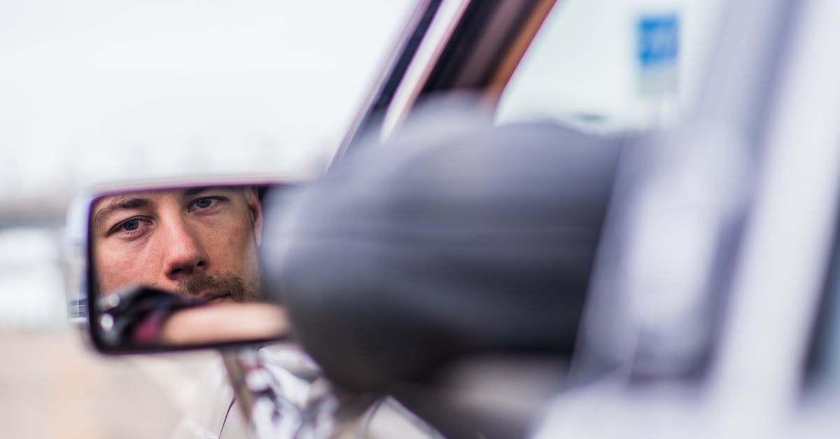 How would I, as a lone driver, operate a parking barrier when driving abroad on a different side of the road? - Male driver in car looking in side mirror