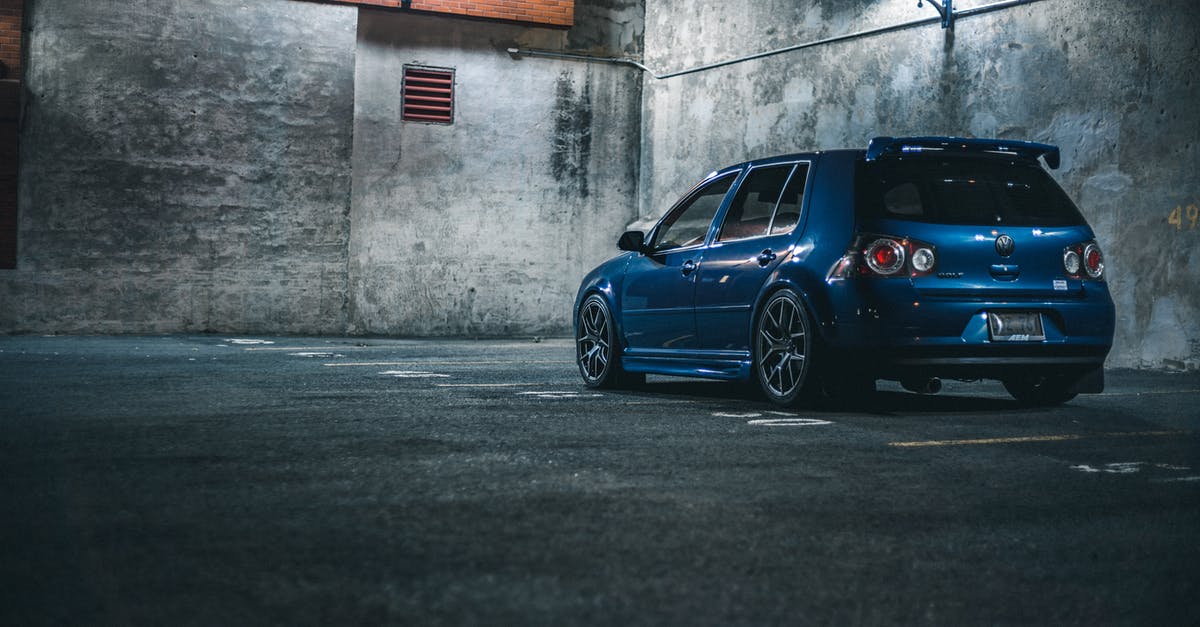 How would I, as a lone driver, operate a parking barrier when driving abroad on a different side of the road? - Blue hatchback automobile with spoiler parked on asphalt with marking lines near stone barrier in city street in evening time