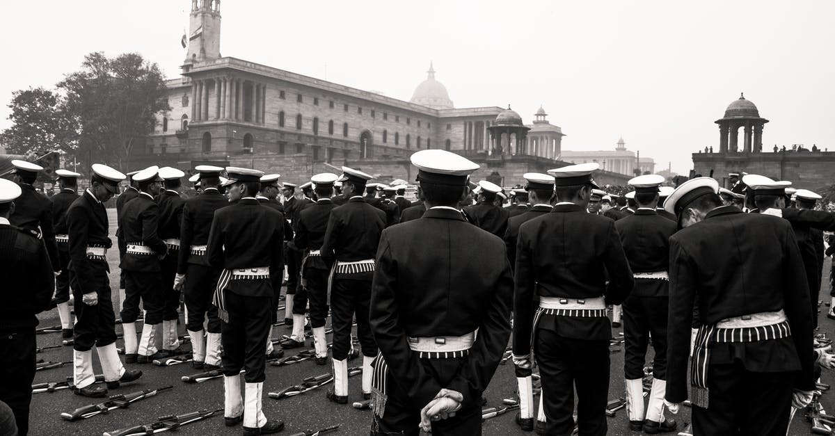 I am a military spouse and I have a friend who is a veteran if we both show our military IDs is my friend allowed to come with me through security - Black and white multiethnic men in military uniform standing in rows near automatic guns lying on ground during military parade on square near old buildings with turrets on daytime