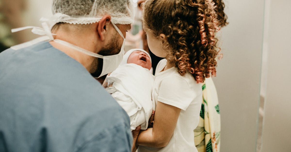 I am applying for a UK Visitor Visa. Can I plan to give birth in an NHS hospital (paying for it), or must I deliver in a fully private hospital? - Man and Child Holding Baby