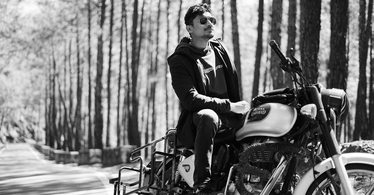 I have a cool suitcase. Might be tricky to ride a motorbike. Looking for a strap allowing to carrying it as a backpack? - Black and white pensive man in sunglasses sitting on stylish motorcycle in sunny forest